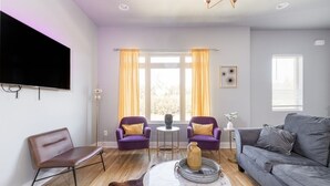 A modern living room with a flat-screen TV, two purple armchairs, a grey sofa, a marble coffee table, and a large window with curtains. - Tailgater's Dream! Rooftop w/ TV + Fire + Lights (Nashville)