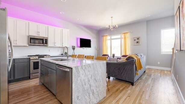 A modern kitchen with a marble island, stainless steel appliances, and a dining area with a sofa and cushions. - Tailgater's Dream! Rooftop w/ TV + Fire + Lights (Nashville)