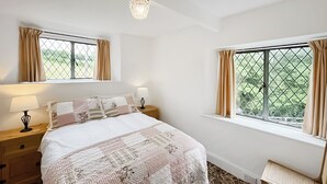 A bedroom with a large bed, two bedside tables, a window with curtains, and a patterned carpet. - 2 bedroom accommodation in Llanarmon-Yn-Ial (Llanarmon-Yn-Ial)