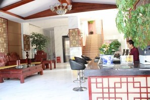 A modern hotel lobby with a reception desk, bar area, seating, and decorative elements like plants and traditional screens. - Ruili Tianhong Hotel (Ruili)