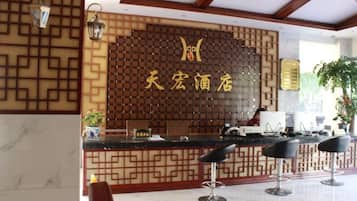 Uma área de recepção com painel de parede de madeira, um balcão de atendimento e três banquetas de bar.