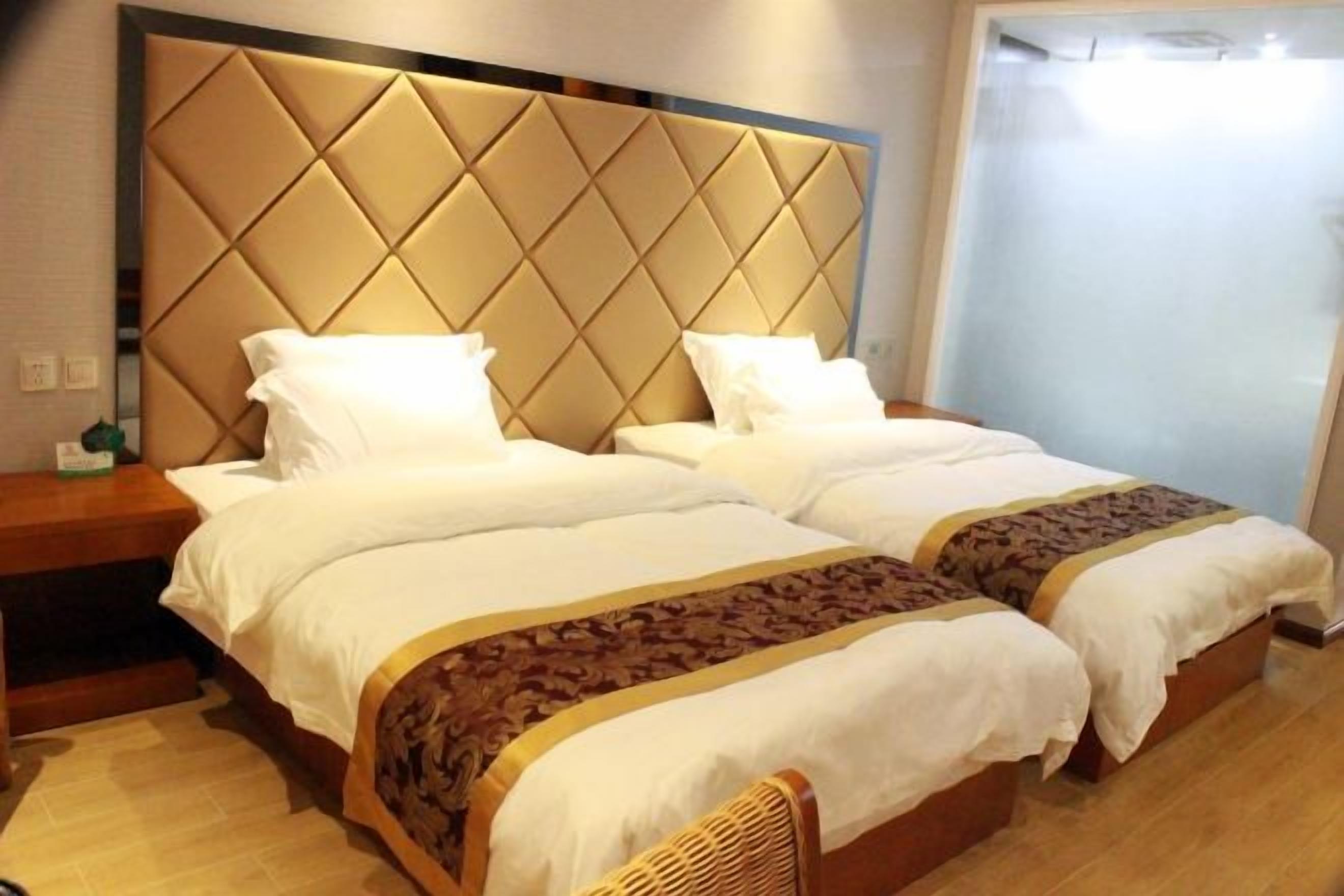 Uma cama de casal com cabeceira acolchoada, duas mesas de cabeceira e um cobreleito estampado.