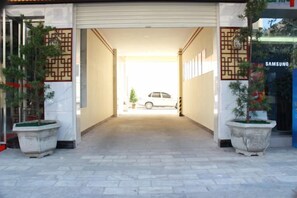 A garage entrance with a white car parked inside, potted plants on either side, and a Samsung store in the background. - Ruili Tianhong Hotel (Ruili)