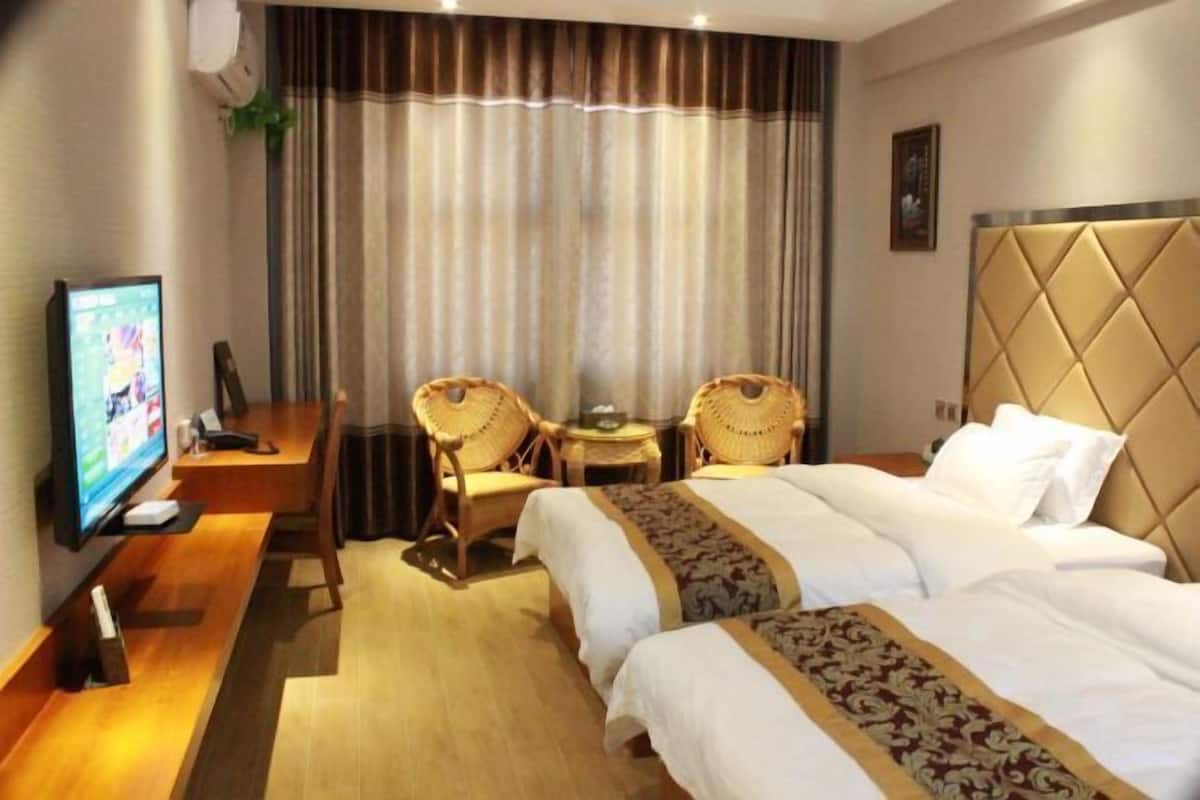 A hotel room with two beds, a desk with a television, and two wicker chairs.