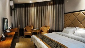 A hotel room with a bed, two chairs, a desk, a television, and a large window with curtains. - Ruili Tianhong Hotel (Ruili)