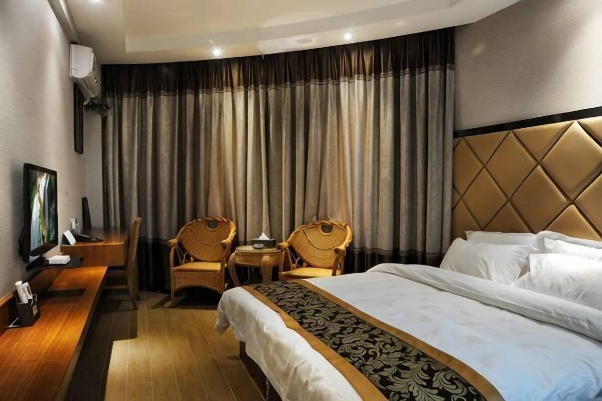 A hotel room with a bed, two chairs, a desk, a television, and a large window with curtains.