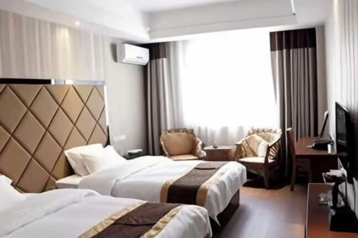 A hotel room with two beds, a TV, a desk, and a seating area with a chair and a sofa.