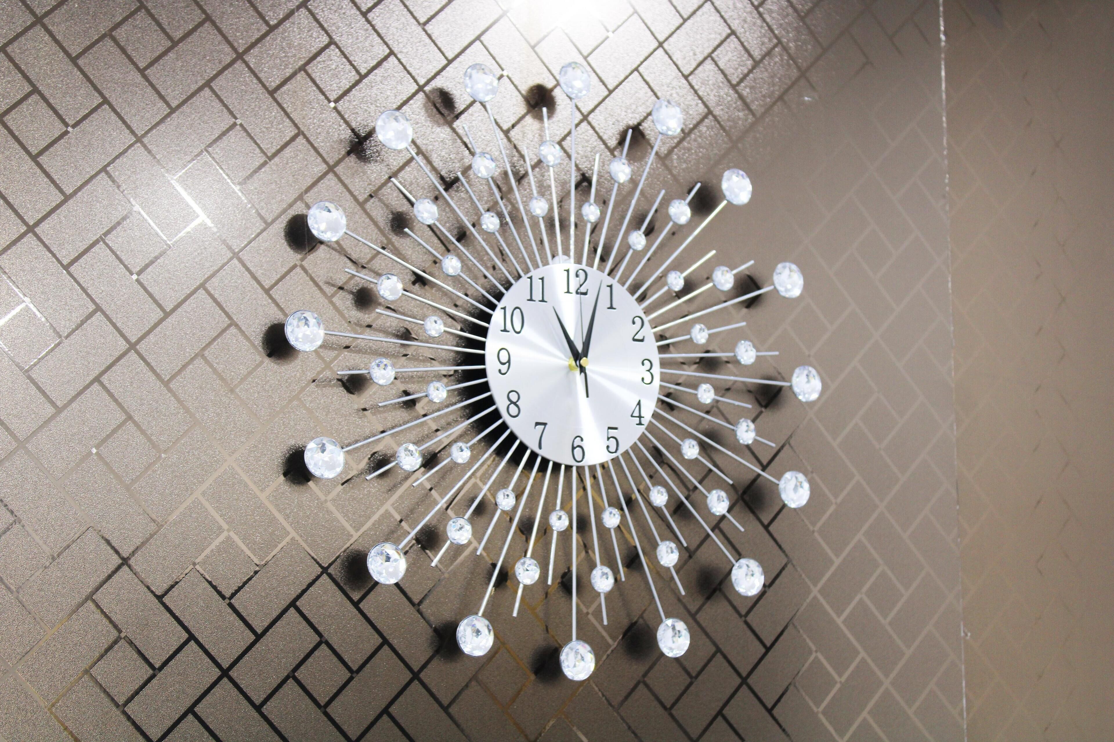Un reloj de pared con diseño de sol y múltiples adornos tipo cristal.