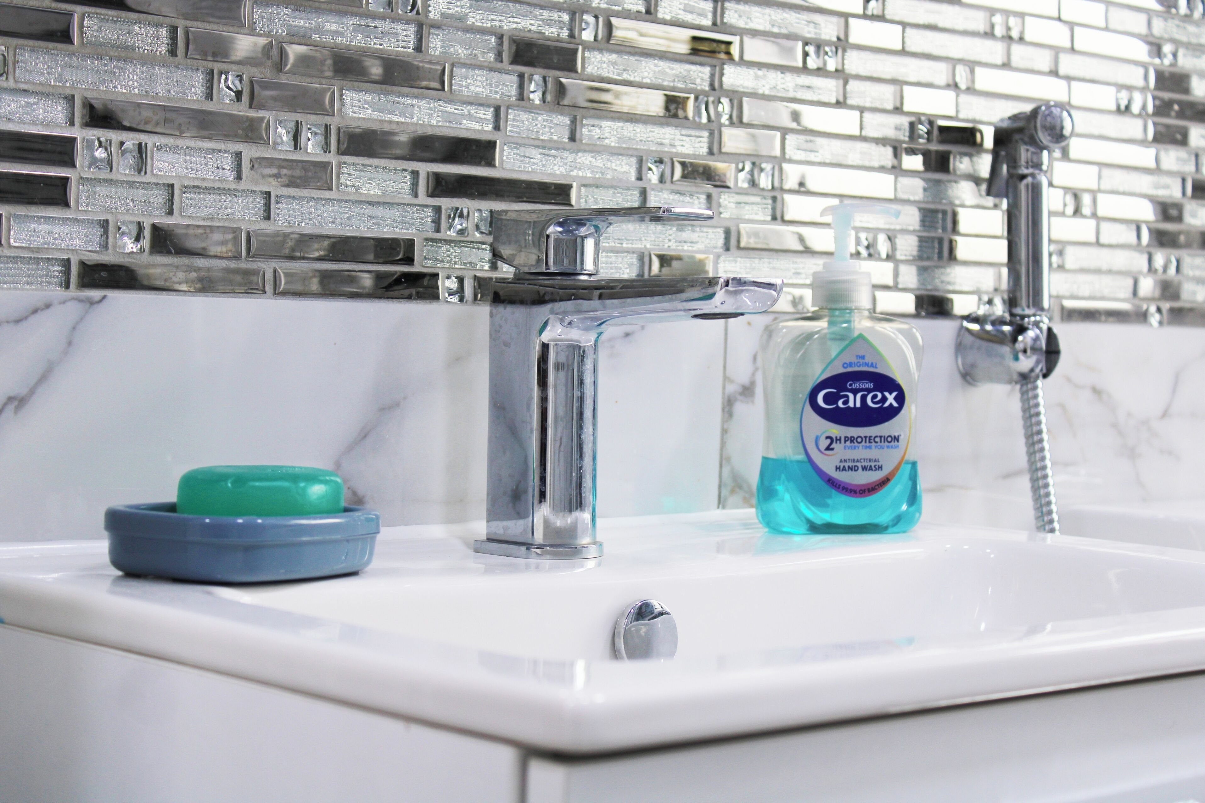 A bathroom sink with a chrome faucet, a soap dish, and a bottle of Carex hand soap.