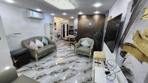 Un salon moderne comprenant un canapé, des fauteuils, une table basse et un téléviseur. La pièce est dotée d’un sol en marbre et d’un élément décoratif mural.