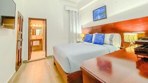 Une chambre d’hôtel avec un lit, un bureau, un miroir, un tableau au mur et une porte donnant sur une salle de bain.