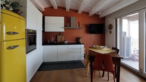 A modern kitchen with a yellow refrigerator, white cabinets, and a black countertop. A dining table with chairs is near a large window.