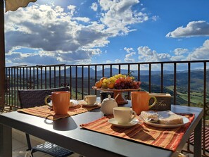 Un balcon avec une table mise pour le petit-déjeuner, comprenant une assiette de fruits, des tasses et un petit pain.