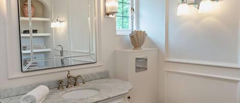 A bathroom with a white vanity, a sink, a mirror, a toilet, and wall-mounted lighting.