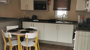 Een kleine keuken met een eettafel en stoelen, een magnetron, een spoelbak en kastjes.
