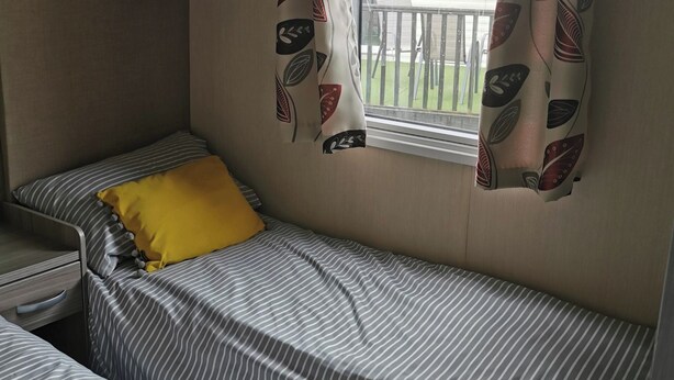 Een kleine kamer met een enkel bed, strepen op het beddengoed en een geel kussen.