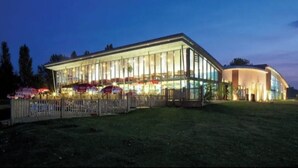 Een modern gebouw met grote glasramen en een plat dak, omgeven door een omheind gebied met parasols.