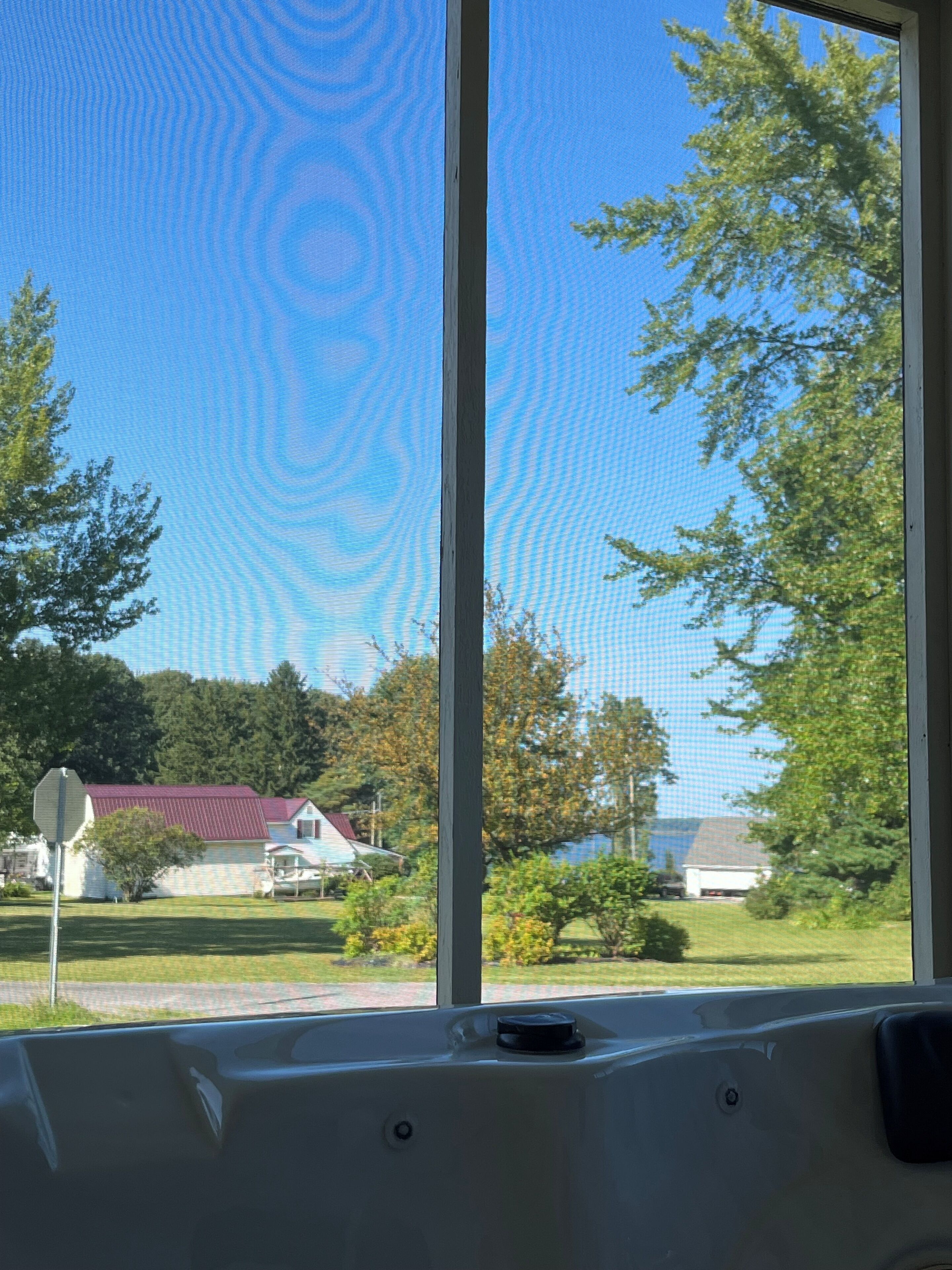 A window with a view of a house, trees, and a clear blue sky.