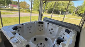 A hot tub with multiple jets, a control panel, and a view of a residential area through large windows.