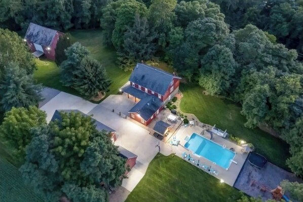 Residential property with a main house surrounded by lush greenery and a swimming pool area.