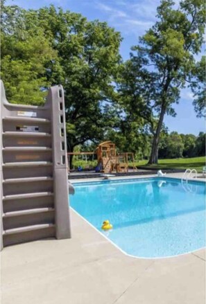 Enjoy a refreshing swim in our pool surrounded by lush greenery and a fun play structure.