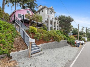 Two-story residence with a pink facade, featuring a staircase and landscaped area with shrubs and a tree.