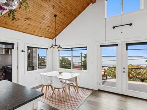 Enjoy a bright and airy space with a high ceiling, dining area, and kitchen, offering views of the outdoors and a body of water.