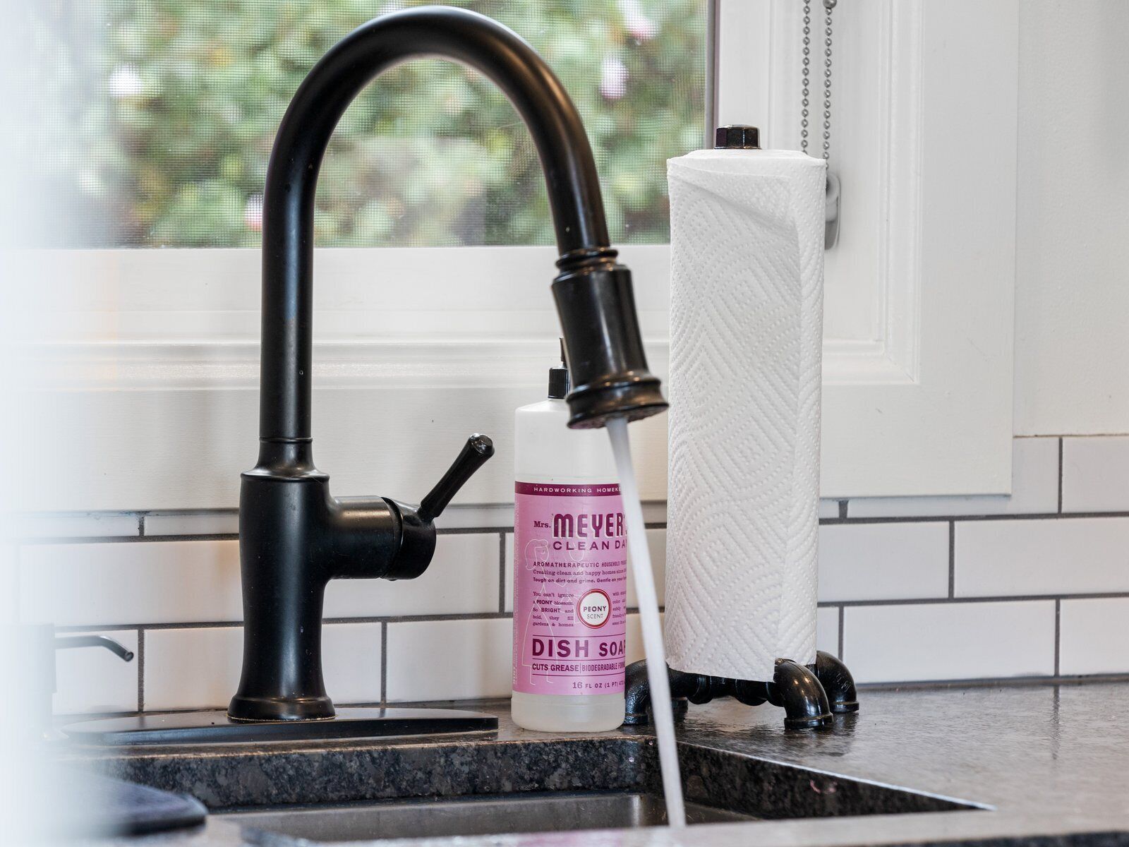 A kitchen sink with a black faucet, a bottle of dish soap, and a paper towel dispenser.