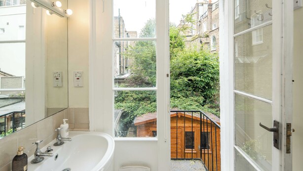 Une salle de bain avec un grand miroir, un lavabo et une fenêtre donnant sur un jardin et des bâtiments.