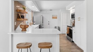 A modern kitchen with white cabinetry, a stainless steel refrigerator, and a wooden island with stools. - PAR-TEE|3bd Golf Course Home - Sleeps 11, Pets OK! (Sarasota)