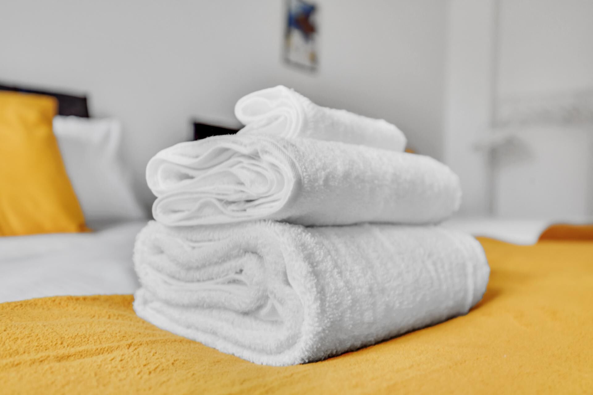 A neatly folded stack of white towels on a bed with a yellow bedspread.