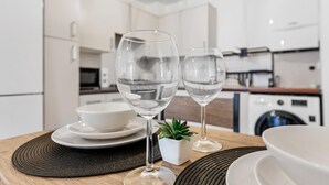 A modern kitchen with white cabinets, a microwave, and a stove. There are two wine glasses on a wooden table with a placemat. - Modern 2-bed Apartment in Stratford (London)
