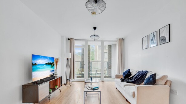 A modern living room with a flat-screen TV, a sofa, a coffee table, and a floor lamp. - Modern 2-bed Apartment in Stratford (London)