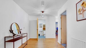 A hallway with wooden flooring, a mirror on a console table, a ceiling fan, and a framed picture on the wall. - Modern 2-bed Apartment in Stratford (London)