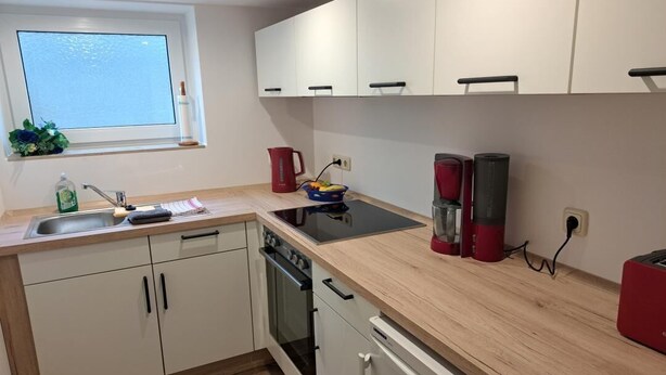A modern kitchen with white cabinets, a wooden countertop, a built-in oven, and a window above the sink.