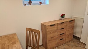 A wooden dining table with a chair, a wooden cabinet with drawers, a small window with a view, and a radiator.
