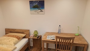 A bedroom with a bed, a desk, a chair, a nightstand, and a painting on the wall.