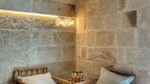 Una habitación rústica con paredes de piedra, dos sillas de madera y una pequeña mesa con dos copas doradas.