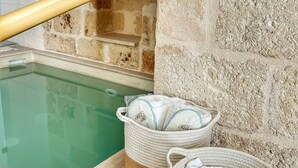 Una zona de piscina con un columpio de madera, dos cestas tejidas con toallas y un muro de piedra.