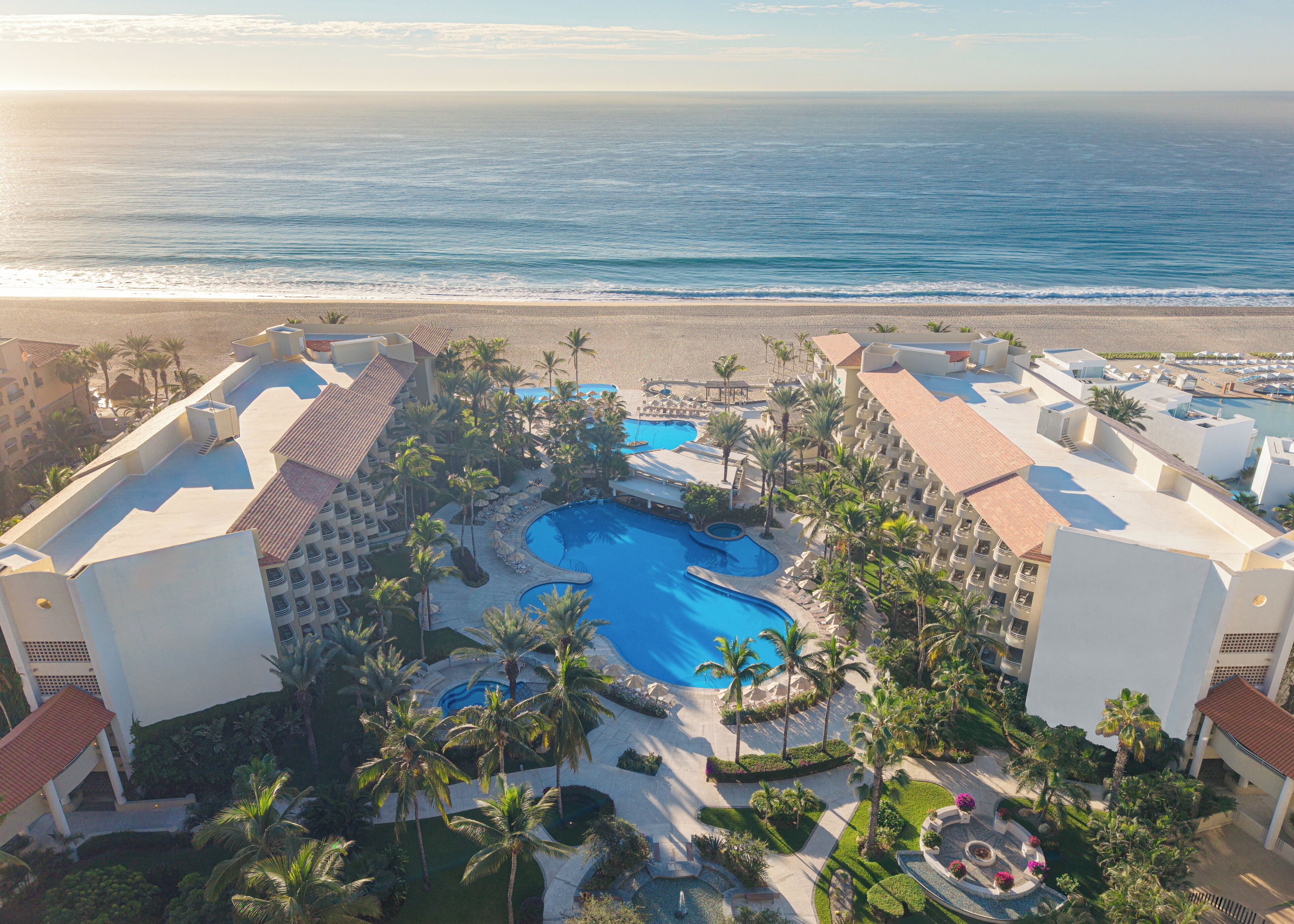 A resort with multiple swimming pools, palm trees, and a beach view.