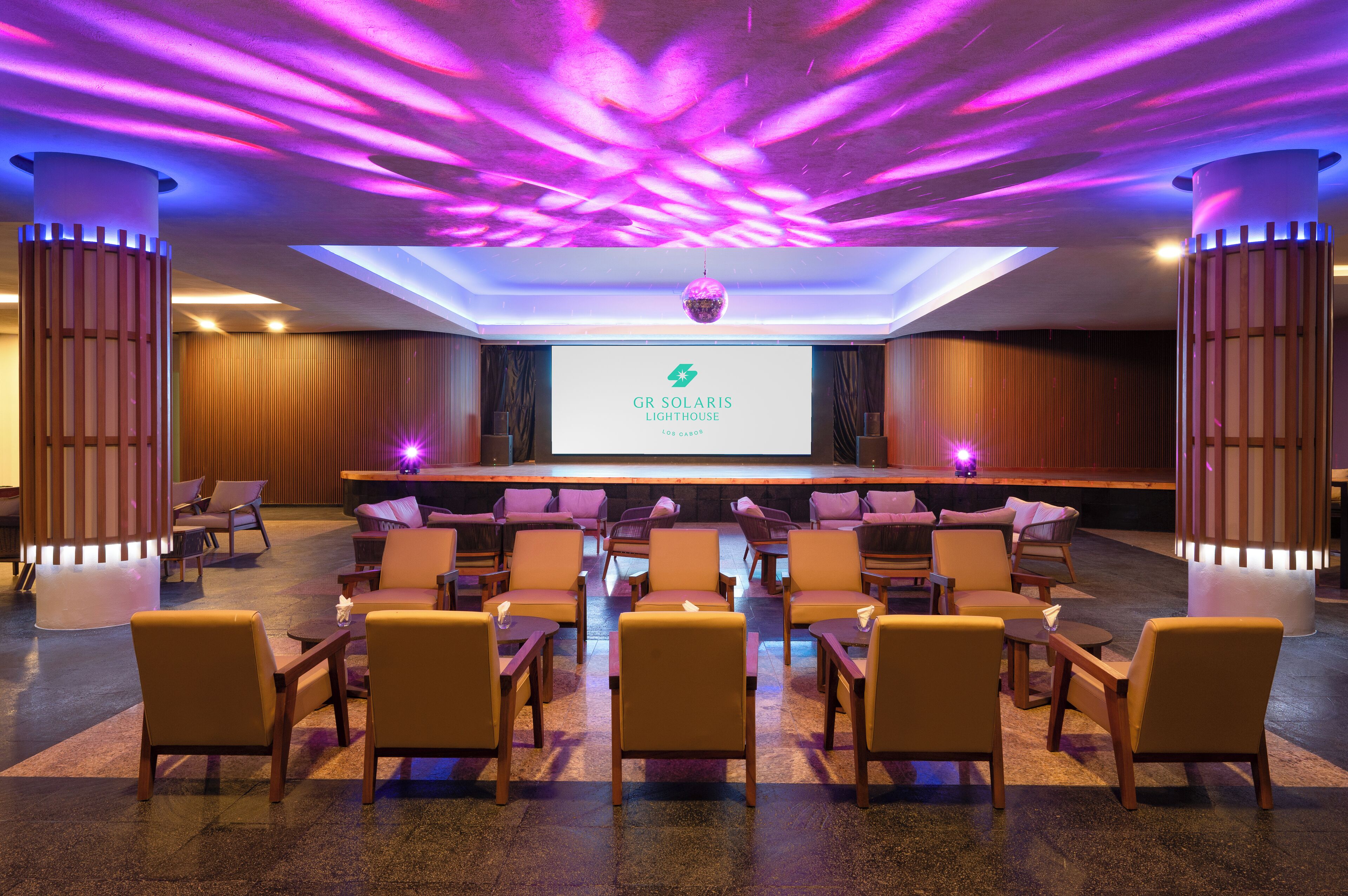 A conference room with a stage, chairs, and a screen displaying the GR SOLARIS Lighthouse logo.