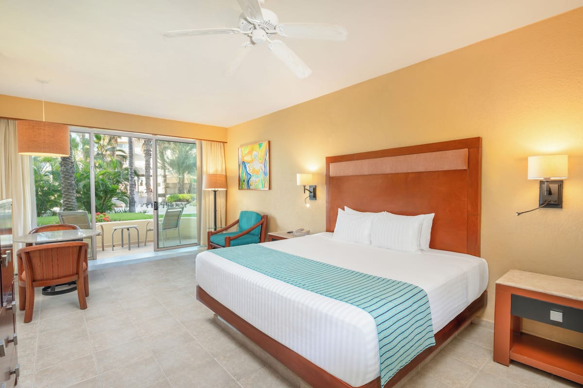 A hotel room with a large bed, a desk with a chair, a ceiling fan, and a view of the outdoors.