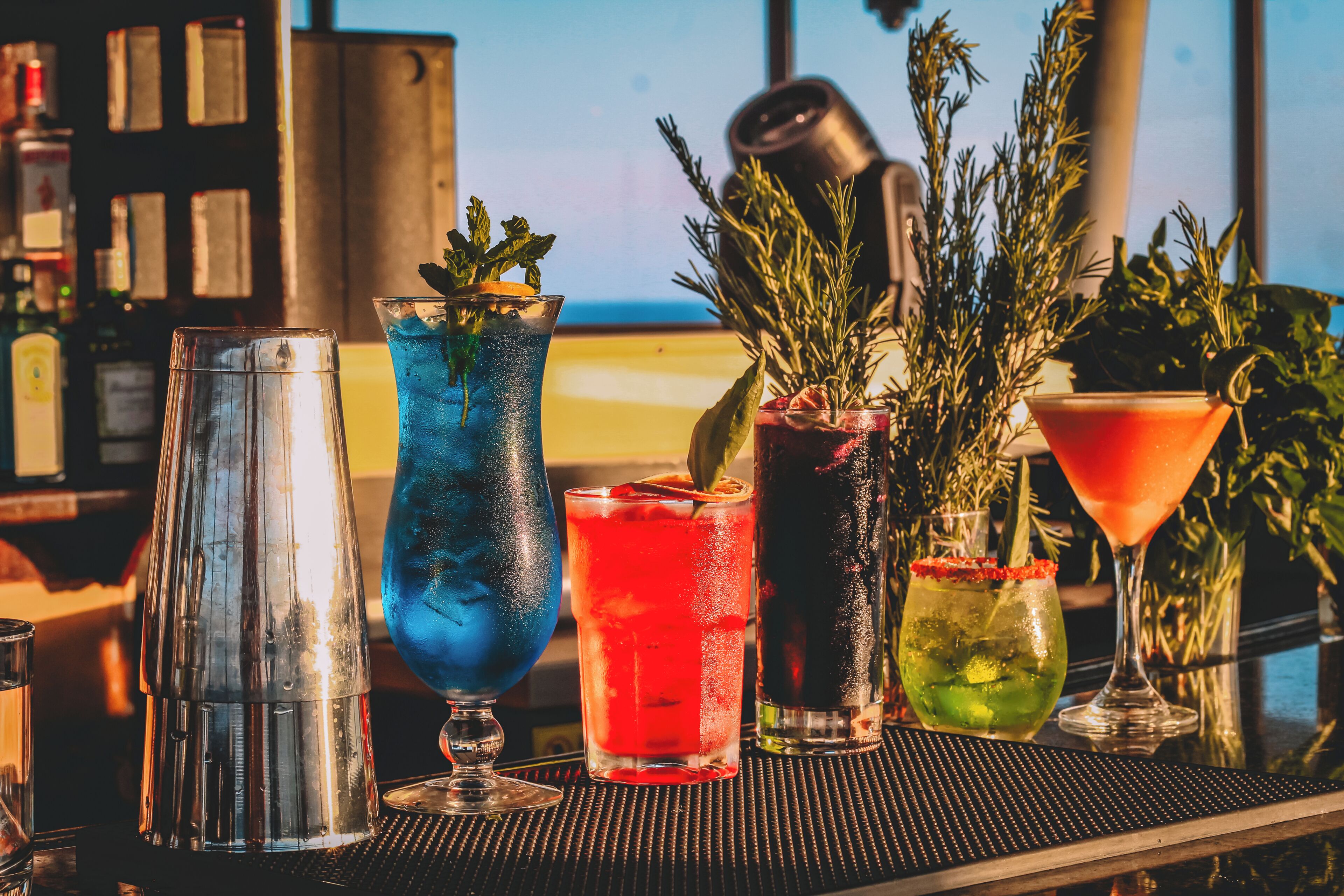 A bar with various drinks, a cocktail shaker, and a potted plant.