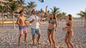 A group of people on a sandy beach with palm trees and a building in the background. - GR Solaris Lighthouse Los Cabos (San José del Cabo)