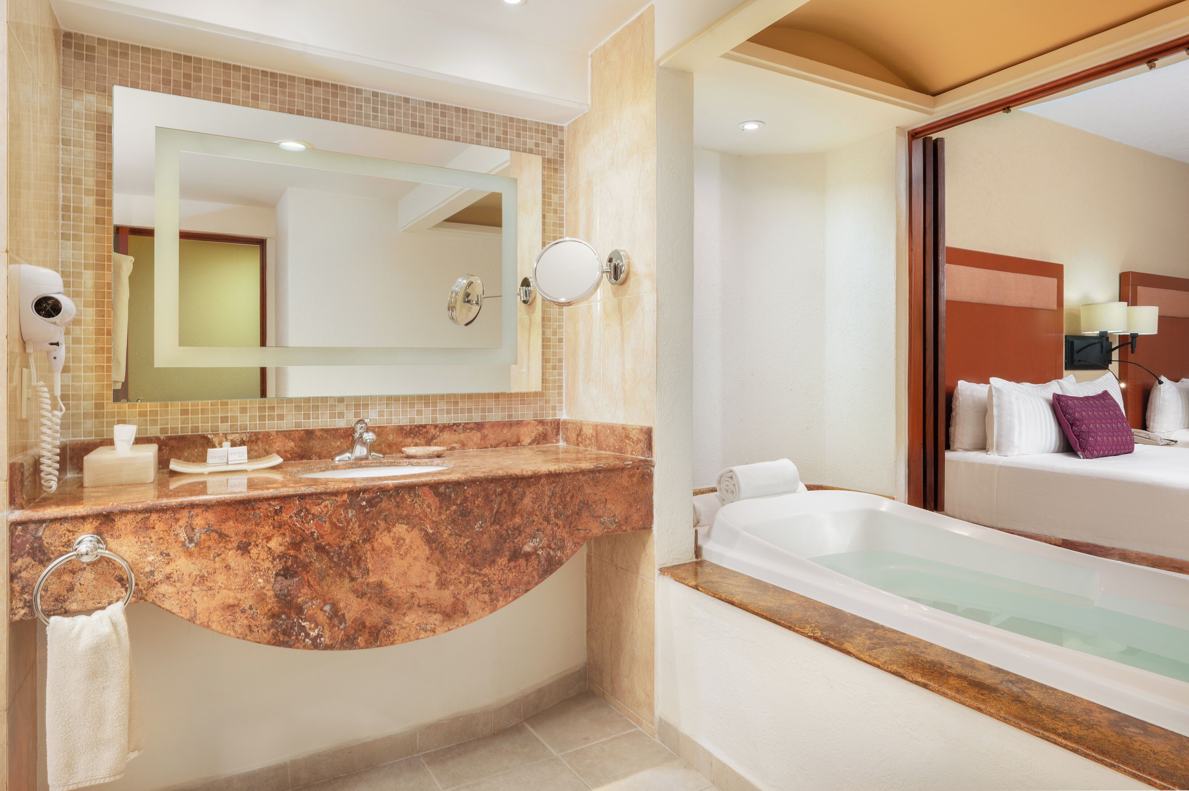 Un baño moderno con lavamanos de mármol, un espejo grande, una bañera empotrada y un secador de pelo en la pared.