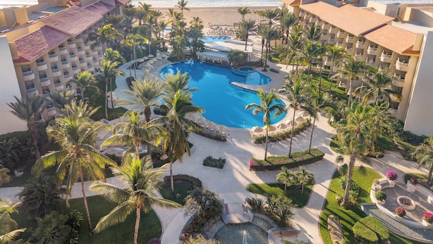 A resort with a central pool, palm trees, and a view of the ocean. - GR Solaris Lighthouse Los Cabos (San José del Cabo)