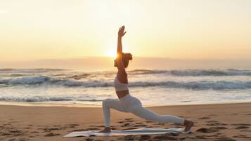 Eine Person führt eine Yoga-Pose an einem Strand mit Blick auf das Meer aus.