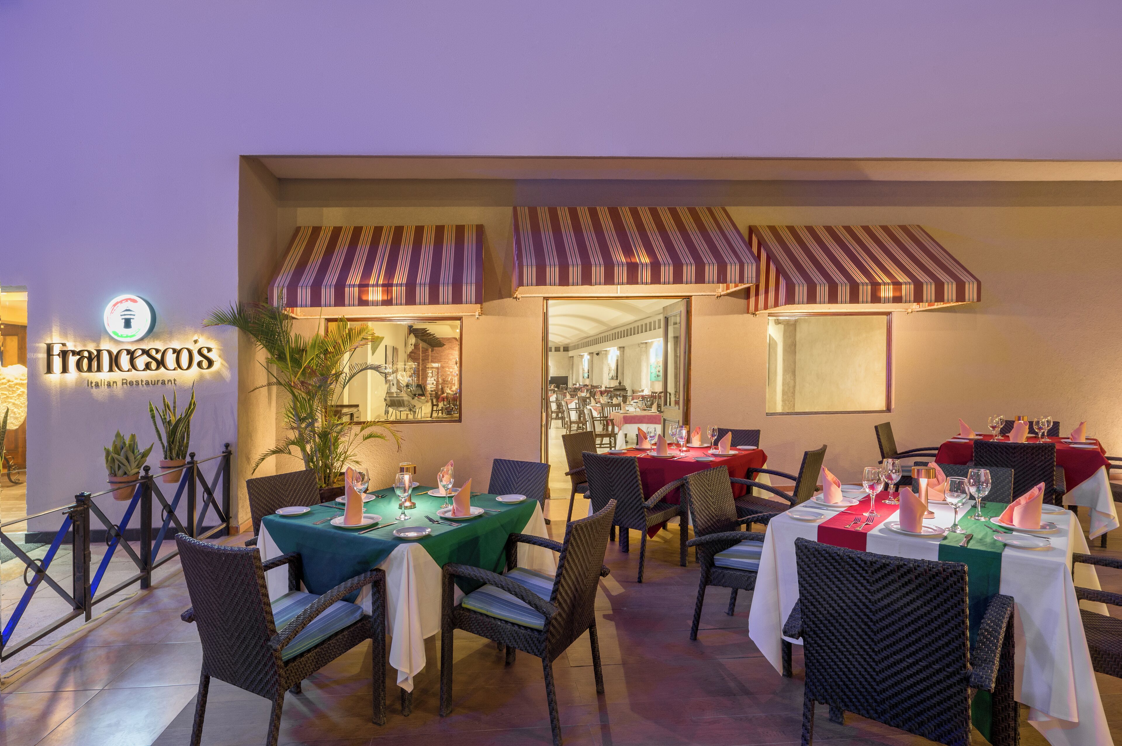 An outdoor dining area of Francesco's Italian Restaurant with tables set for dining, striped awnings, and potted plants.