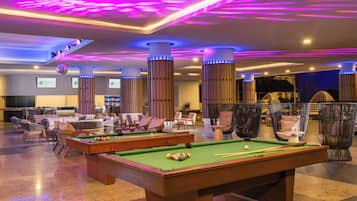 A pool table in a well-lit room with modern furniture and a bar area in the background.