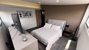 A modern bedroom with a large bed, a desk with a computer, and a standing fan. - Amplio apt en poblado by Hoost APT 701 (Medellín)